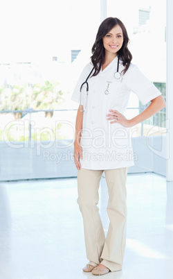 Young smiling nurse standing upright with one hand on her hip