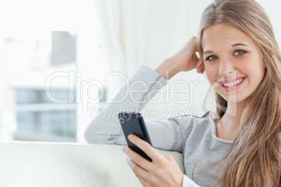 A smiling girl with a phone in hand as she looks at the camera