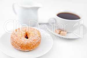 Doughnut with icing sugar and a cup of coffee on white plates wi