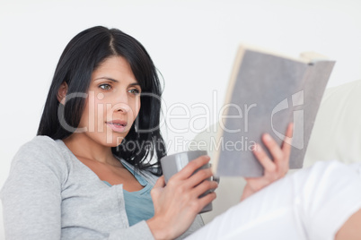 Woman holding a grey mug while reading a book