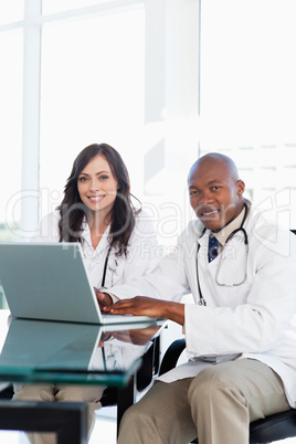 Smiling doctor working on a laptop while accompanied by his coll