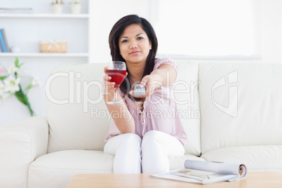 Woman holds a glass of wine and a television remote