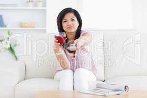 Woman holds a glass of wine and a television remote