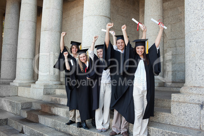 Five happy graduates posing the arms raised
