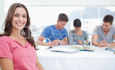 A smiling woman sits in front of her three friends who are study