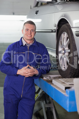 Front view of a smiling mechanic next to a car