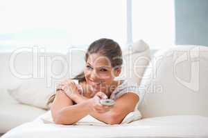 Woman lying on a sofa while pointing with a remote