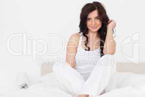 Smiling brunette woman sitting on her bed with legs crossed