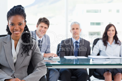 Serious businesswoman sitting in front of her team while smiling