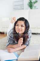 Thinking woman lying on the floor with a book and a notebook