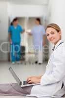 Woman doctor sitting on the floor while typing on a laptop