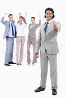 Businessman smiling with his thumbs up and cheering people behin