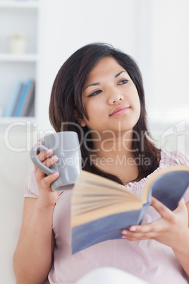 Woman sitting on a couch while holding a book and a mug