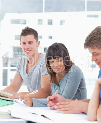 A man smiles while his friends beside him study