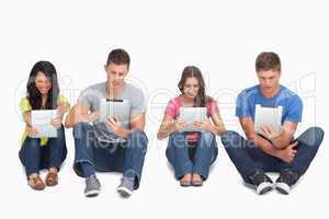 Four people sitting beside each other using their tablets