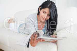 Woman lying on a sofa while holding a magazine
