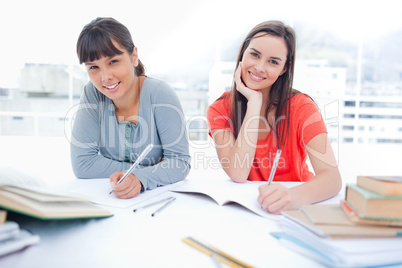 Two girls smiling and looking into the camera as they do homewor