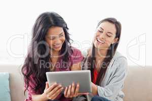 A laughing pair of women on the couch watching their tablet pc