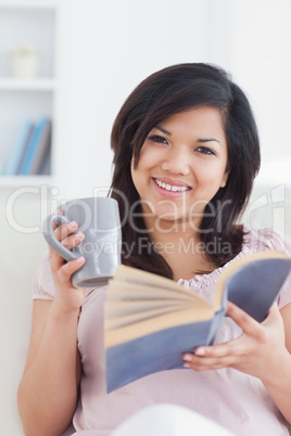 Woman smiling while holding a mug and a book