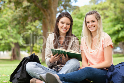 Smiling teenagers sitting while studying with a textbook