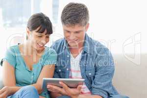 A smiling couple sit on the couch and use a tablet