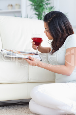 Woman holding up a glass of red wine while reading a magazine