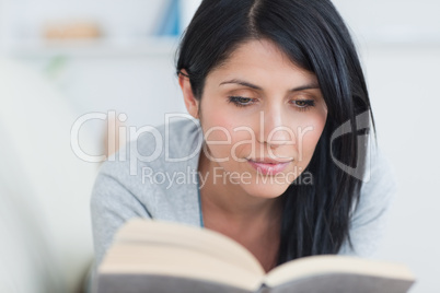 Woman reading a book while lying on a white couch