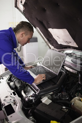 Mechanic looking at a computer on a car engine