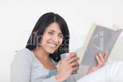 Woman  smiling while reading a book and holding a mug