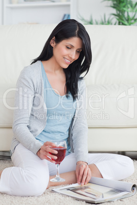 Smiling woman turning pages of a magazine while holding a glass
