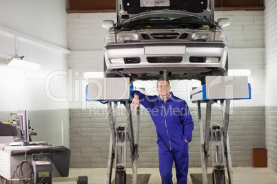 Smiling mechanic leaning on a machine below a car