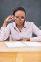 Teacher sitting at desk while touching her glasses