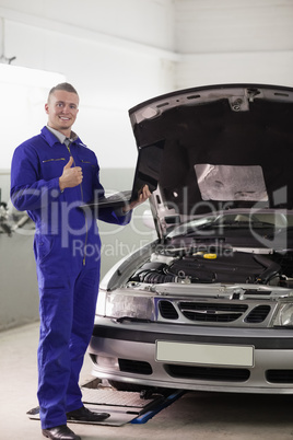 Smiling mechanic holding a computer with thumb up