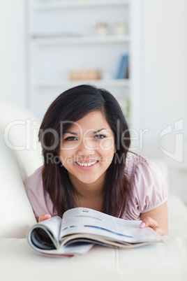 Smiling woman lying on a couch while holding a magazine