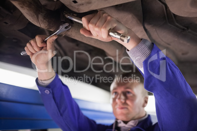 Concentrated mechanic repairing a car while using tools