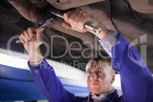 Concentrated mechanic repairing a car while using tools