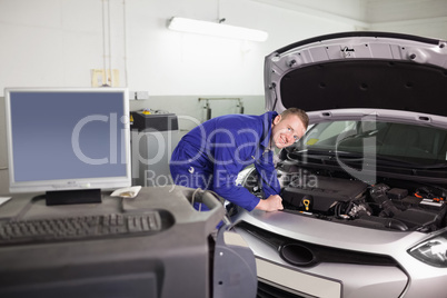 Smiling mechanic examining an engine of a car