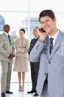 Smiling businessman using a mobile phone in front of his team