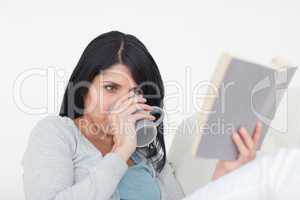 Woman drinking from a grey mug while reading a book