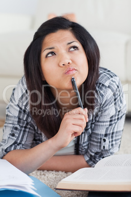 Thinking woman laying on the floor while holding a pen with a bo