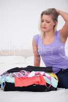 Young woman rubbing her head while looking at her full suitcase