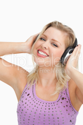 Smiling blonde woman wearing headphones while touching them