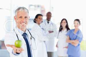 Mature doctor holding an apple while his medical team is looking