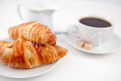 Two croissants and a cup of coffee on white plates with sugar an