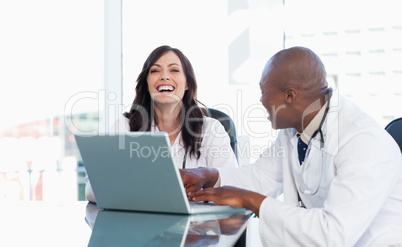 Nurse laughing while working on a laptop with a colleague