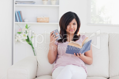 Woman sitting on a sofa while she is holding a mug and a book