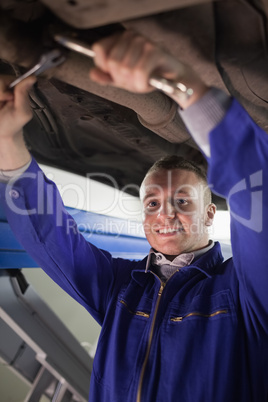 Mechanic repairing a car while looking at camera