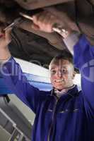 Mechanic repairing a car while looking at camera