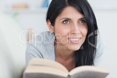 Woman smiling while holding a book and lying on a couch