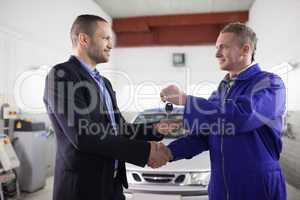 Man receiving car key while shaking hand to a mechanic